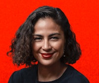 a woman with curly hair and red lipstick is posing in front of a red background